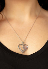 Load image into Gallery viewer, A pink rhinestone encrusted heart intertwines with a plain silver heart inside of a larger silver heart frame, creating a romantic pendant at the bottom of a shimmery silver chain. Features an adjustable clasp closure.  Sold as one individual necklace. Includes one pair of matching earrings. 