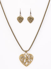 Load image into Gallery viewer, An airy heart swings from the bottom of a shimmery brass cocoon chain, creating a whimsical pendant below the collar. Brushed in an antiqued shimmer, frilly filigree climbs the heart frame for a vintage inspired finish. Features an adjustable clasp closure.  Sold as one individual necklace. Includes one pair of matching earrings.