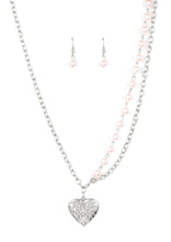Load image into Gallery viewer, Swirling with filigree details, a whimsical heart pendant swings from the bottom of a shimmery silver chain below the collar. A single strand of pearly pink beads drape down one side for a refined asymmetrical finish. Features an adjustable clasp closure.  Sold as one individual necklace. Includes one pair of matching earrings.