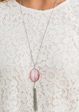 Load image into Gallery viewer, An oversized pink cat's eye stone frame gives way to a shimmery silver chain tassel, creating a whimsically stacked pendant at the bottom of a lengthened silver chain. Features an adjustable clasp closure.  Sold as one individual necklace. Includes one pair of matching earrings.