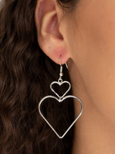 Load image into Gallery viewer, A large silver heart silhouette swings from the bottom of a dainty silver heart silhouette, creating a charming lure. Earring attaches to a standard fishhook fitting.  