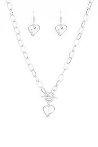 Cut into a whimsical heart shape, a glittery white gem swings from the bottom of a glistening silver chain below the collar for a charming look. Features a toggle closure.  Sold as one individual necklace. Includes one pair of matching earrings.  