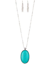 Load image into Gallery viewer, Chiseled into a tranquil oval, a dramatically over sized turquoise stone pendant swings from the bottom of a lengthened silver chain. Glassy white rhinestones dust the pendant&#39;s fitting for a refined flair. Features an adjustable clasp closure.  Sold as one individual necklace. Includes one pair of matching earrings.