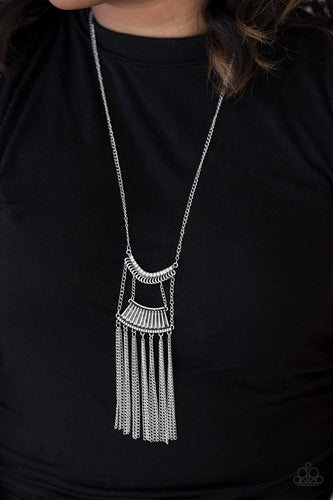 Encrusted in glittery white rhinestones, a bowing silver pendant attaches to an ornate silver frame, creating a bold pendant. Infused with an elongated silver chain, the tribal inspired pendant gives way to a shimmery silver fringe for a fierce finish. Features an adjustable clasp closure.  Sold as one individual necklace. Includes one pair of matching earrings.  Always nickel and lead free.