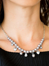 Load image into Gallery viewer, Shimmery silver heart charms, silver beads, and silver pearls swing from a row of matching silver pearls, creating a whimsical fringe below the collar. Featuring a regal teardrop shape, a glittery white rhinestone swings from the center for a refined finish. Features an adjustable clasp closure.  Sold as one individual necklace. Includes one pair of matching earrings. 