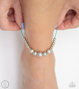 A collection of dainty silver and hammered silver beads slide along a shiny turquoise cord around the ankle for a whimsical look. Features an adjustable sliding knot closure.  Sold as one individual anklet.  Always nickel and lead free.