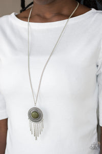 An earthy green stone is pressed into the center of a shimmery silver disc radiating with glistening tribal details. Swinging from the bottom of a lengthened silver chain, the bold pendant gives way to a fringe of delicately hammered silver rods for a wanderlust finish. Features an adjustable clasp closure.  Sold as one individual necklace. Includes one pair of matching earrings.  Always nickel and lead free.