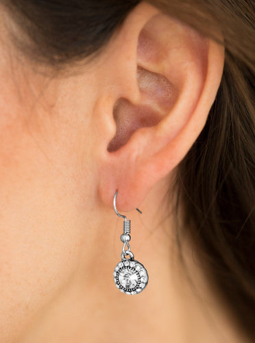 A glittery white rhinestone is pressed into a dainty silver frame. Dazzling white rhinestones are sprinkled around the beaming center, adding a refined shimmer to the timeless frame. Earring attaches to a standard fishhook fitting.  Sold as one pair of earrings.