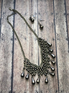 Threaded along metallic rods, stacked brass beads give way to shimmery teardrops. The edgy fringe flawlessly drapes beneath the collar, creating a sassy tapered fringe. Features an adjustable clasp closure.  Sold as one individual necklace. Includes one pair of matching earrings.