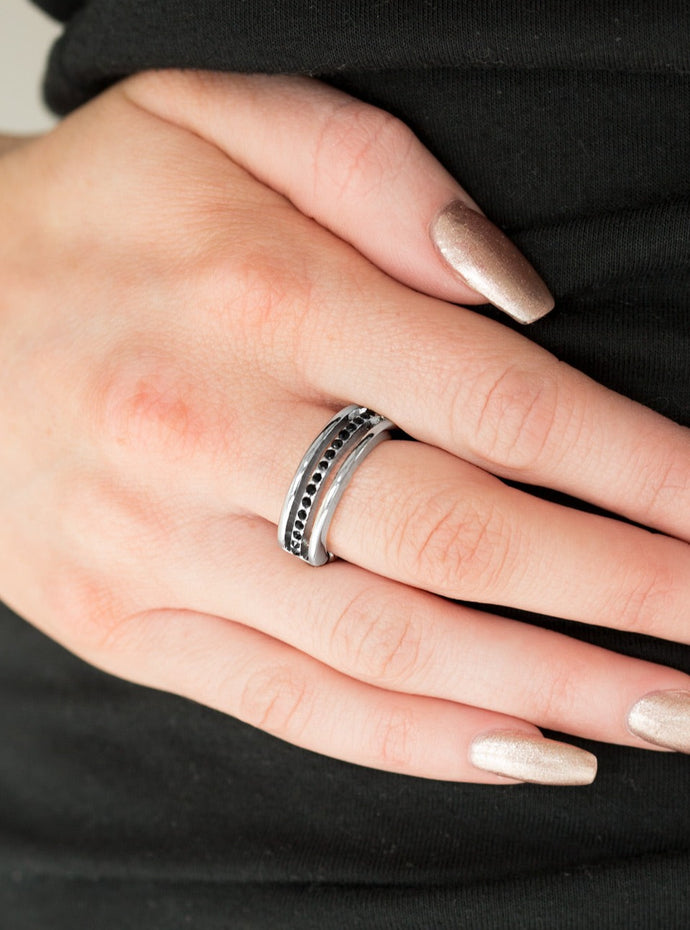 Dainty silver bands layer across the finger. The center most band is encrusted in black rhinestones for a glamorous finish. Features a dainty stretchy band for a flexible fit.  Sold as one individual ring. 