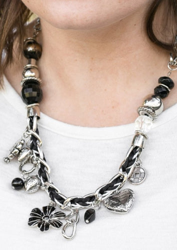 Black and ivory cording is braided through a chunky silver chain. A unique variety of charms decorate the piece including a delicate flower and a heart. Heart is inscribed with the phrase 
