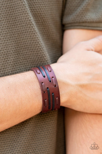 Brown and black leather laces are haphazardly threaded through a thick brown leather band, creating a rustic display around the wrist. Features an adjustable snap closure.  Sold as one individual bracelet.  Always nickel and lead free. 