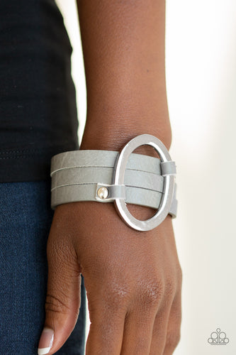 An oval silver ring loops through two belt loop fittings and is studded in place across the front of a spliced gray leather band for a bold urban look. Features an adjustable snap closure.  Sold as one individual bracelet.  Always nickel and lead free.