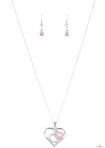 A pink rhinestone encrusted heart intertwines with a plain silver heart inside of a larger silver heart frame, creating a romantic pendant at the bottom of a shimmery silver chain. Features an adjustable clasp closure.  Sold as one individual necklace. Includes one pair of matching earrings.