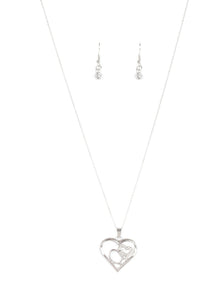A white rhinestone encrusted heart intertwines with a plain silver heart inside of a larger silver heart frame, creating a romantic pendant at the bottom of a shimmery silver chain. Features an adjustable clasp closure.  Sold as one individual necklace. Includes one pair of matching earrings.