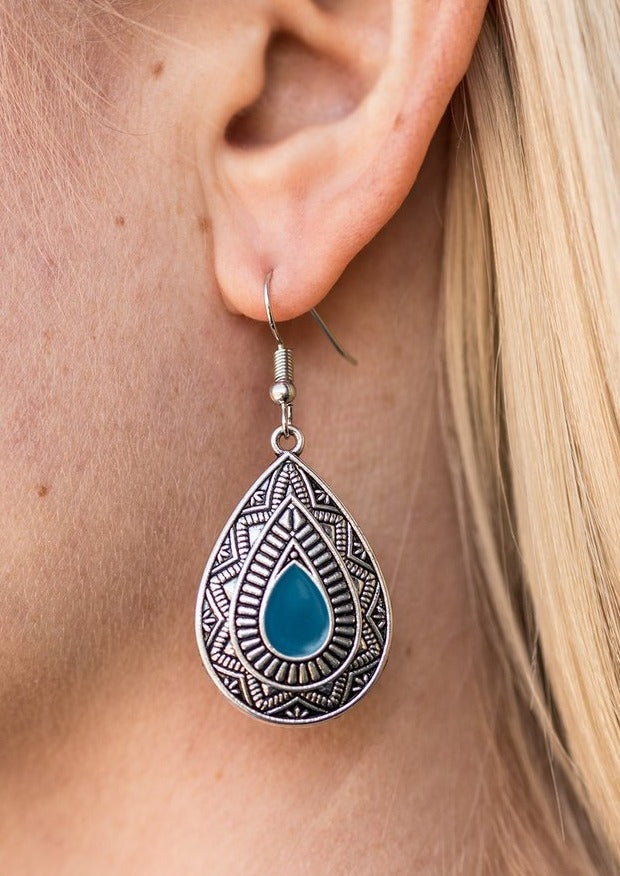 Painted in a blue center, an ornate teardrop embossed in tribal inspired textures swings from the ear in an indigenous fashion. Earring attaches to a standard fishhook fitting.  Sold as one pair of earrings.