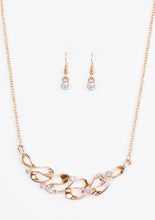 Load image into Gallery viewer, A ribbon of glistening gold loops below the collar, creating a refined pendant. White rhinestones are sprinkled along the rippling ribbons, adding a classic sparkle to the timeless pendant. Features an adjustable clasp closure.  Sold as one individual necklace. Includes one pair of matching earrings.