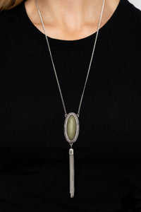 An oval Military Olive stone is pressed into a glistening silver frame stamped in antiqued tribal inspired patterns. A shimmery silver chain tassel swings from the bottom of the earthy pendant for a whimsical finish. Features an adjustable clasp closure.  Sold as one individual necklace. Includes one pair of matching earrings.  