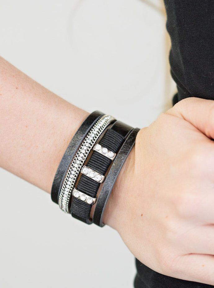 Metallic black leather strands layer across the wrist. Infused with silver chain and white rhinestone accents, black cording knots around a leather strand, securing glittery white rhinestone frames in place for a sassy finish. Features an adjustable clasp closure.  Sold as one individual bracelet.