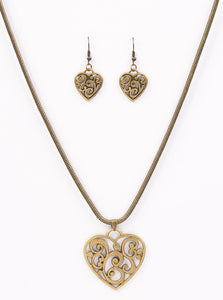 An airy heart swings from the bottom of a shimmery brass cocoon chain, creating a whimsical pendant below the collar. Brushed in an antiqued shimmer, frilly filigree climbs the heart frame for a vintage inspired finish. Features an adjustable clasp closure.  Sold as one individual necklace. Includes one pair of matching earrings. 