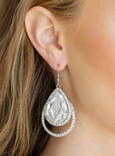 A dramatically over sized white teardrop gem is pressed into a doubled silver frame encrusted in countless white rhinestones for a blinding look. Earring attaches to a standard fishhook fitting.  Sold as one pair of earrings.