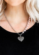 Load image into Gallery viewer, Swirling with filigree details, a whimsical heart pendant swings from the bottom of a shimmery silver chain below the collar. A single strand of pearly pink beads drape down one side for a refined asymmetrical finish. Features an adjustable clasp closure.  Sold as one individual necklace. Includes one pair of matching earrings. 