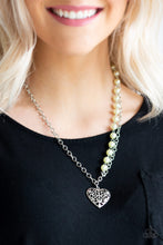 Load image into Gallery viewer, Swirling with filigree details, a whimsical heart pendant swings from the bottom of a shimmery silver chain below the collar. A single strand of pearly yellow beads drape down one side for a refined asymmetrical finish. Features an adjustable clasp closure.  Sold as one individual necklace. Includes one pair of matching earrings.  Always nickel and lead free
