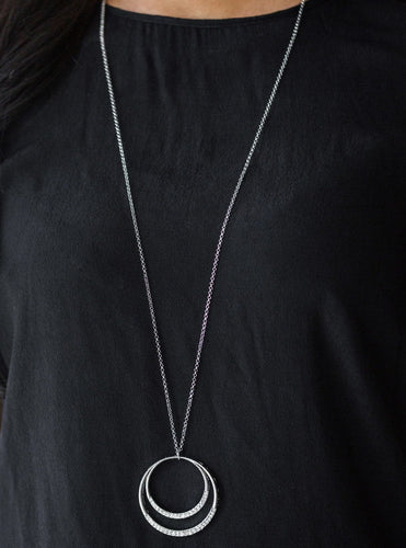 A daring circular pendant swings from the bottom of an elongated silver chain for a refined look. The bottoms of the ornate silver pendant are encrusted in white rhinestones for a glamorous finish. Features an adjustable clasp closure.  Sold as one individual necklace. Includes one pair of matching earrings. 