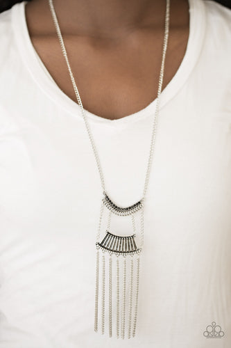 Encrusted in glittery black rhinestones, a bowing silver pendant attaches to an ornate silver frame, creating a bold pendant. Infused with an elongated silver chain, the tribal inspired pendant gives way to a shimmery silver fringe for a fierce finish. Features an adjustable clasp closure.  Sold as one individual necklace. Includes one pair of matching earrings.  Always nickel and lead free.
