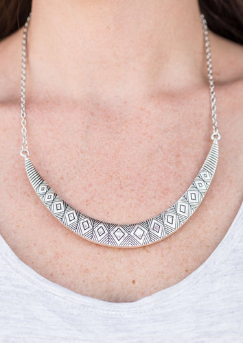 Stamped in tribal inspired patterns, a silver crescent-shaped plate swings from the bottom of a shimmery silver chain, creating a bold pendant below the collar. Features an adjustable clasp closure.   Sold as one individual necklace. Includes one pair of matching earrings.  