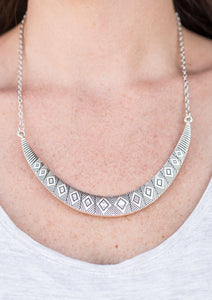 Stamped in tribal inspired patterns, a silver crescent-shaped plate swings from the bottom of a shimmery silver chain, creating a bold pendant below the collar. Features an adjustable clasp closure.   Sold as one individual necklace. Includes one pair of matching earrings.  