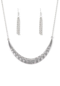 Stamped in tribal inspired patterns, a silver crescent-shaped plate swings from the bottom of a shimmery silver chain, creating a bold pendant below the collar. Features an adjustable clasp closure.   Sold as one individual necklace. Includes one pair of matching earrings.