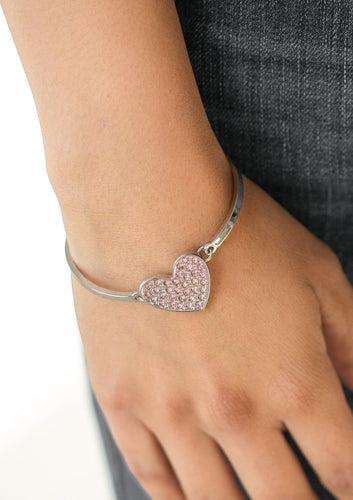 A pink rhinestone encrusted silver heart frame delicately links to two dainty silver bars arcing around the wrist, creating a dazzling centerpiece. Features an adjustable clasp closure.  Sold as one individual bracelet.  