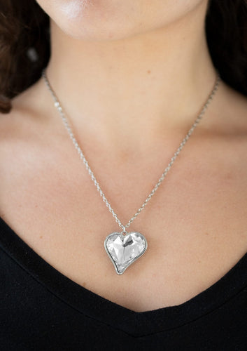 Chiseled into a charming heart, an over sized white rhinestone gem is nestled inside a sleek silver frame, creating a flirtatious pendant below the collar. Features an adjustable clasp closure.  Sold as one individual necklace. Includes one pair of matching earrings.  