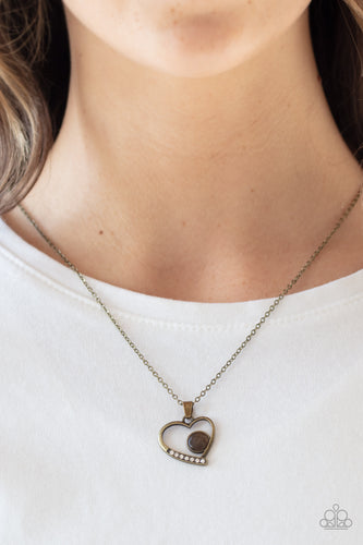 A dainty brown cat's eye stone is nestled inside of a brass heart frame. The bottom of the pendant is encrusted in a section of glassy white rhinestones, creating a romantic pendant below the collar. Features an adjustable clasp closure.  Sold as one individual necklace. Includes one pair of matching earrings. Always nickel and lead free.