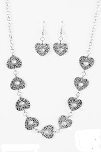 Vintage inspired heart frames link below the collar, creating a whimsical chain. Brushed in an antiqued finish, shiny filigree delicately climbs the silver hearts for an ornate finish. Features an adjustable clasp closure.  Sold as one individual necklace. Includes one pair of matching earrings.