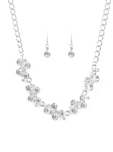 A row of dazzling white rhinestones drapes along the neckline, creating a sparkling display. Daintier white rhinestones are sprinkled along the clusters, adding luminous detail to the timeless design. Features an adjustable clasp closure.  Sold as one individual necklace. Includes one pair of matching earrings.