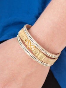 Metallic tan leather strands layer across the wrist. Infused with rows of white rhinestones, tan cording knots around the centermost strand, securing an airy gold heart and infinity charm in place for a whimsical finish. Features an adjustable clasp closure.  Sold as one individual bracelet.