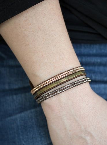 A brown suede band is spliced into three strands featuring rows of glittery hematite rhinestones, flat brass chain, and faceted metallic rhinestones for a glamorous look. Features an adjustable snap closure. Sold as one individual bracelet. 
