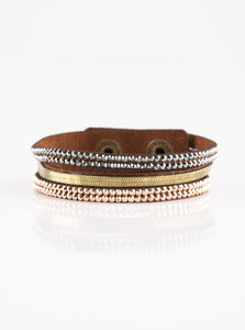 A brown suede band is spliced into three strands featuring rows of glittery hematite rhinestones, flat brass chain, and faceted metallic rhinestones for a glamorous look. Features an adjustable snap closure. Sold as one individual bracelet. 