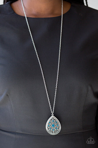 A dramatic teardrop pendant swings from the bottom of an elongated silver chain, elegantly slimming the torso. Glittery blue rhinestones are sprinkled along the pendant as silver filigree dances across the center, creating a regal floral pattern. Features an adjustable clasp closure.  Sold as one individual necklace. Includes one pair of matching earrings.  Always nickel and lead free!