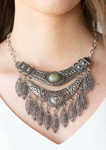 Featuring a collision of hammered, studded, and embossed patterns, two silver half-moon plates dramatically stack below the collar. Swirling with studded filigree detail, ornate silver frames swing from the bottoms of the stacked pendants, creating a fierce tribal inspired fringe. An earthy green stone is pressed into the center of the uppermost frame for a seasonal finish. Features an adjustable clasp closure.  Sold as one individual necklace. Includes one pair of matching earrings.