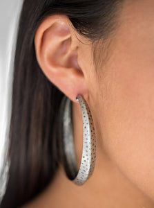 A thick silver hoop creases at the center, creating a chic 3-dimensional display. Finished in a hammered surface, the antiqued design evokes an indigenous inspired style. Earring attaches to standard post fitting. Hoop measures 2 1/4" in diameter.  Sold as one pair of hoop earrings.
