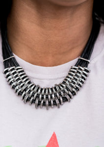 Bold and unapologetic, this hefty necklace gives off a hand-made feel with its multiple strands of black cording held together by industrial silver fittings that shift and slide. Features an adjustable clasp closure.