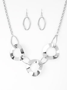 Featuring slightly warped surfaces, asymmetrical silver hoops link with reflective silver rings below the collar for a modern look. Features an adjustable clasp closure.  Sold as one individual necklace. Includes one pair of matching earrings.