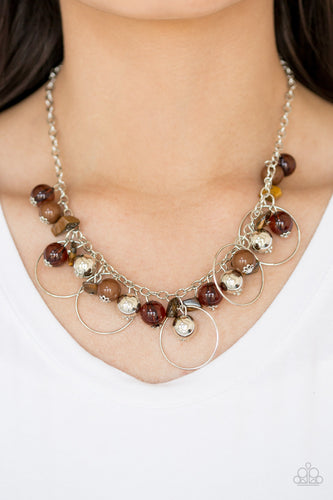 Glassy brown, polished brown, and classic silver chains swing from the bottom of a shimmery silver chain. Infused with large silver hoops, bits of tranquil brown rock beading trickle between the beaded accent, creating an earthy fringe below the collar. Features an adjustable clasp closure.  Sold as one individual necklace. Includes one pair of matching earrings.  Always nickel and lead free.