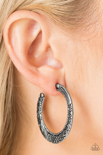 Embossed in tribal inspired patterns, a glistening silver hoop curls around the ear for an indigenous look. Earring attaches to a standard post fitting. Hoop measures 1 1/2