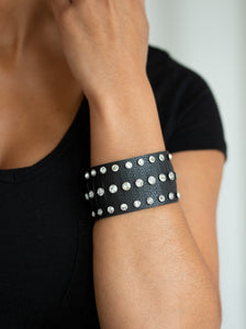 Pressed into sleek silver frames, glittery white rhinestones are studded across a thick black leather band featuring a center lined with slits for a sassy finish. Features an adjustable snap closure.  Sold as one individual bracelet.