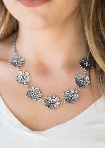 Featuring lifelike detail, a row of shimmery silver flowers links below the collar for a seasonal look. Features an adjustable clasp closure.  Sold as one individual necklace. Includes one pair of matching earrings.