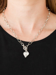 Cut into a whimsical heart shape, a glittery white gem swings from the bottom of a glistening silver chain below the collar for a charming look. Features a toggle closure.  Sold as one individual necklace. Includes one pair of matching earrings.  